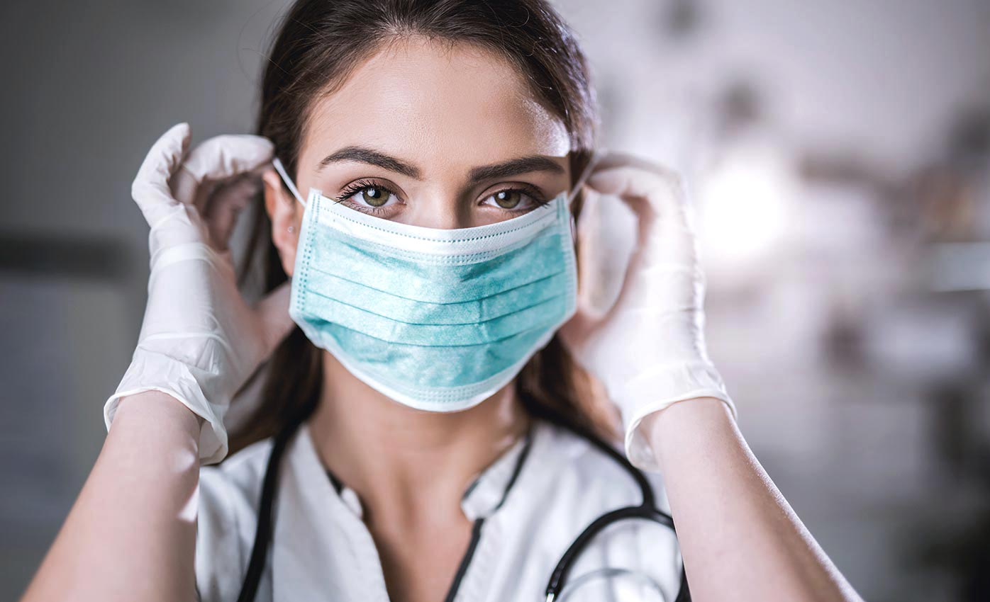 A clinician dons personal protective equipment including a mask