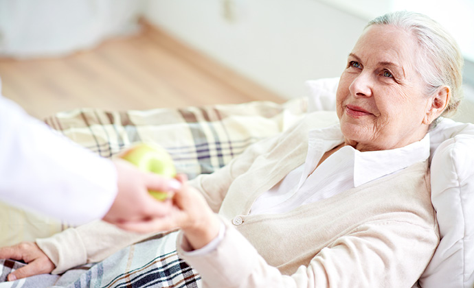 A person hands an apple to a woman, who is seated on a sofa